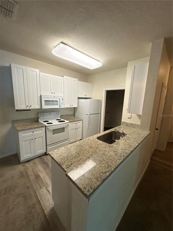 A kitchen features white cabinets, granite countertops, a white stove, and a refrigerator — 8009 HEMINGWAY CIRCLE UNIT 8009, HAINES CITY, FL