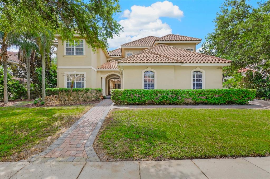 A two-story stucco house with a tile roof, arched entryway, and a brick walkway — 11226 MACAW COURT, WINDERMERE, FL