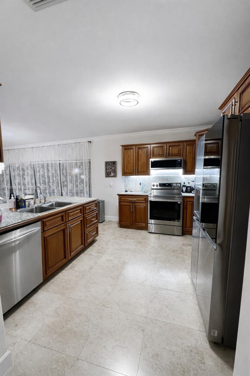 A kitchen features wood cabinets, stainless steel appliances, granite countertops, and light-colored tile flooring — 13451 SW 74th Ave, Pinecrest FL 33156, PINECREST, FL