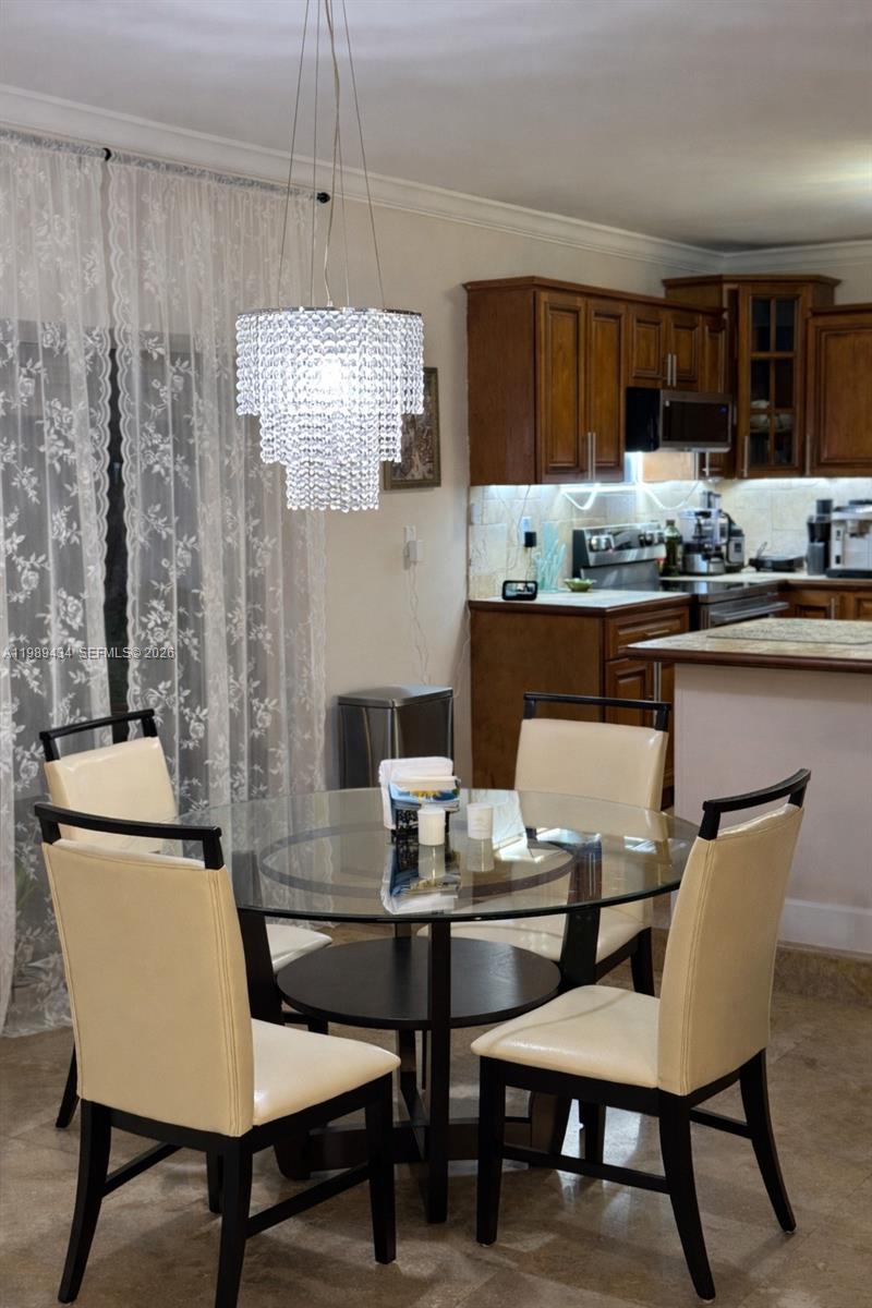 A dining area features a glass-topped table, four chairs, and a crystal chandelier — 13451 SW 74th Ave, Pinecrest FL 33156, PINECREST, FL