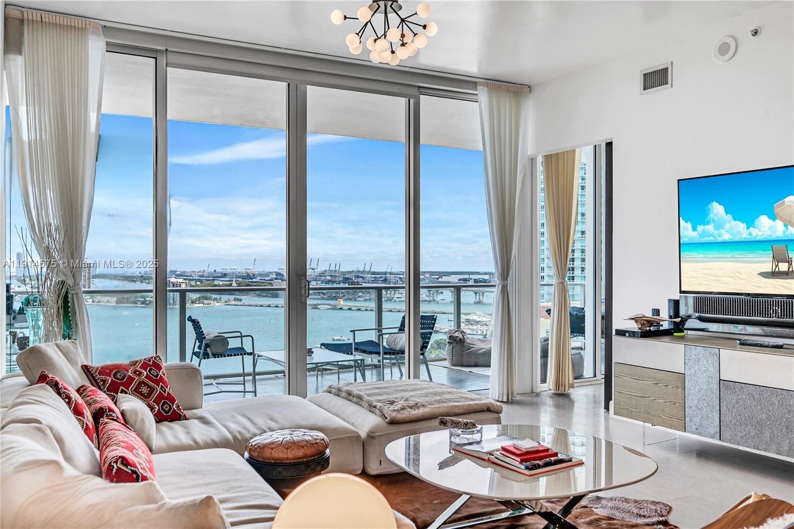 A living room with a sectional sofa, glass coffee table, and floor-to-ceiling windows overlooking water — 2020 N Bayshore Dr # 1906, Miami FL 33137, MIAMI, FL