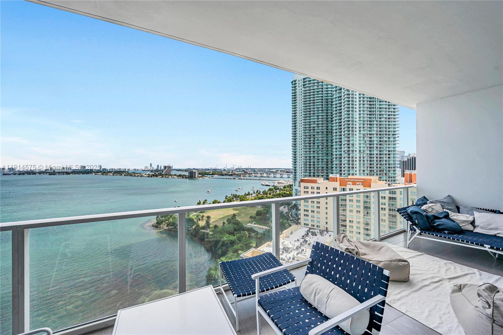 A high-rise balcony features outdoor seating overlooking a bay, a park, and city skyscrapers — 2020 N Bayshore Dr # 1906, Miami FL 33137, MIAMI, FL