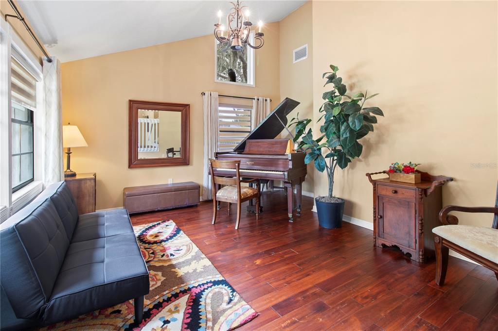 A living room features a grand piano, a black sofa, hardwood floors, and a chandelier — 1279 CORNISH COURT, SARASOTA, FL