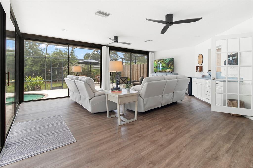 A living room features light wood flooring, white reclining sofas, ceiling fans, and sliding glass doors — 1279 CORNISH COURT, SARASOTA, FL