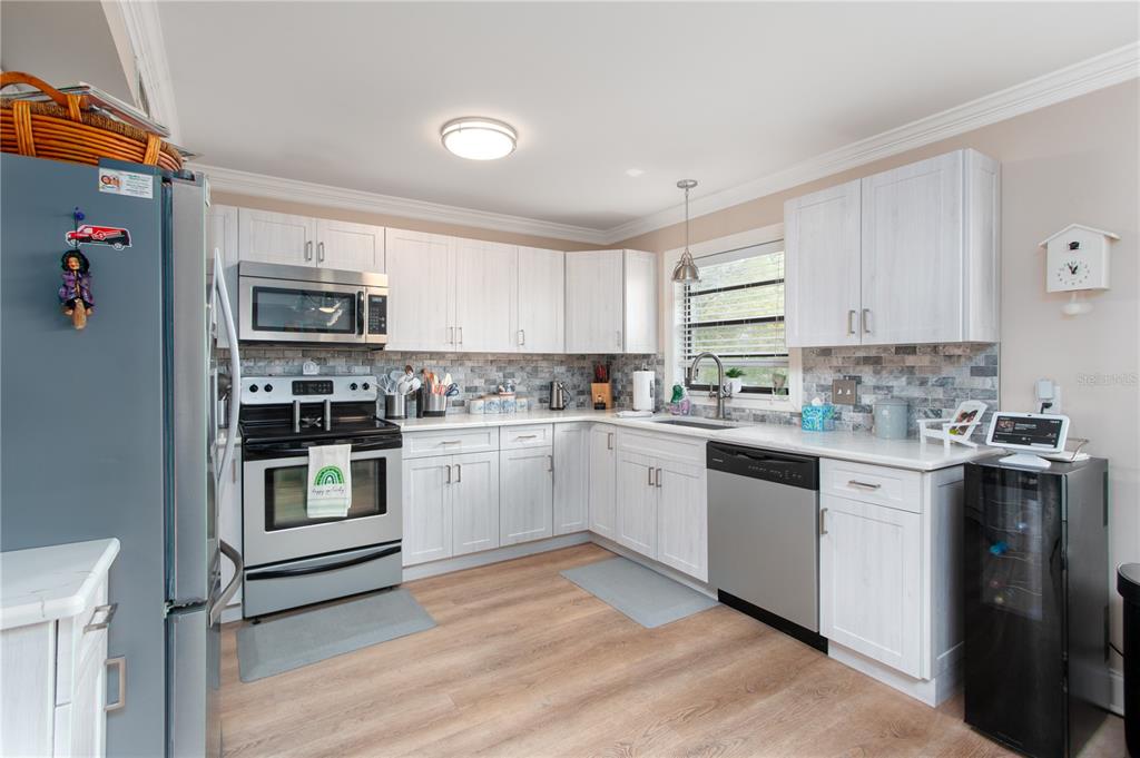 A kitchen features white cabinets, stainless steel appliances, a tiled backsplash, and light wood flooring — 15 TURNER STREET UNIT 4, CLEARWATER, FL