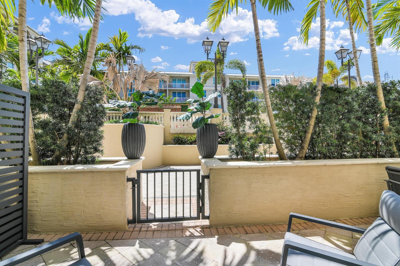 A patio with a metal gate, potted plants, and outdoor seating overlooking a resort building — 99 SE Mizner Boulevard # 612, Boca Raton FL 33432, BOCA RATON, FL