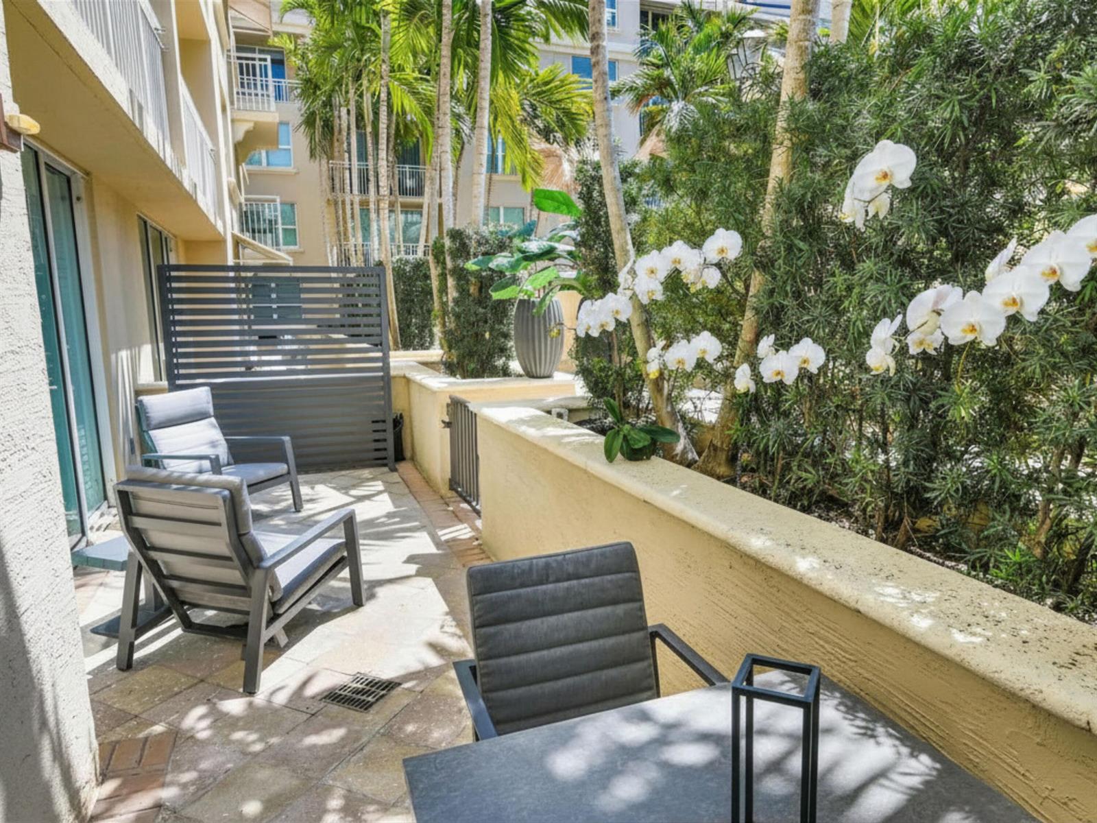 A patio with gray chairs, a small table, and white orchids along a low wall — 99 SE Mizner Boulevard # 612, Boca Raton FL 33432, BOCA RATON, FL