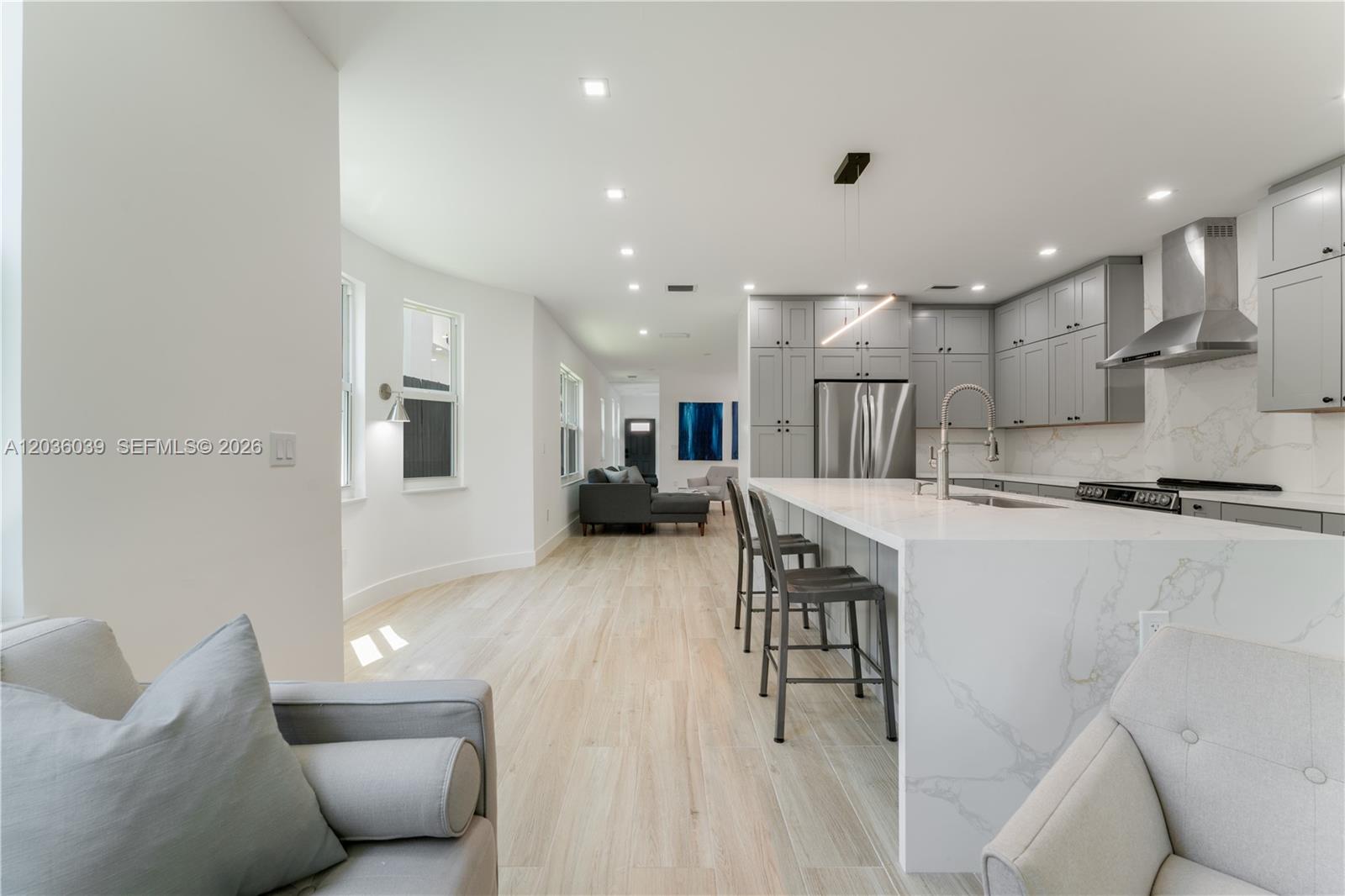 A modern open-concept kitchen features gray cabinetry, a marble waterfall island, and light wood flooring — 3125 Paola Dr # 15, Miami FL 33133, MIAMI, FL
