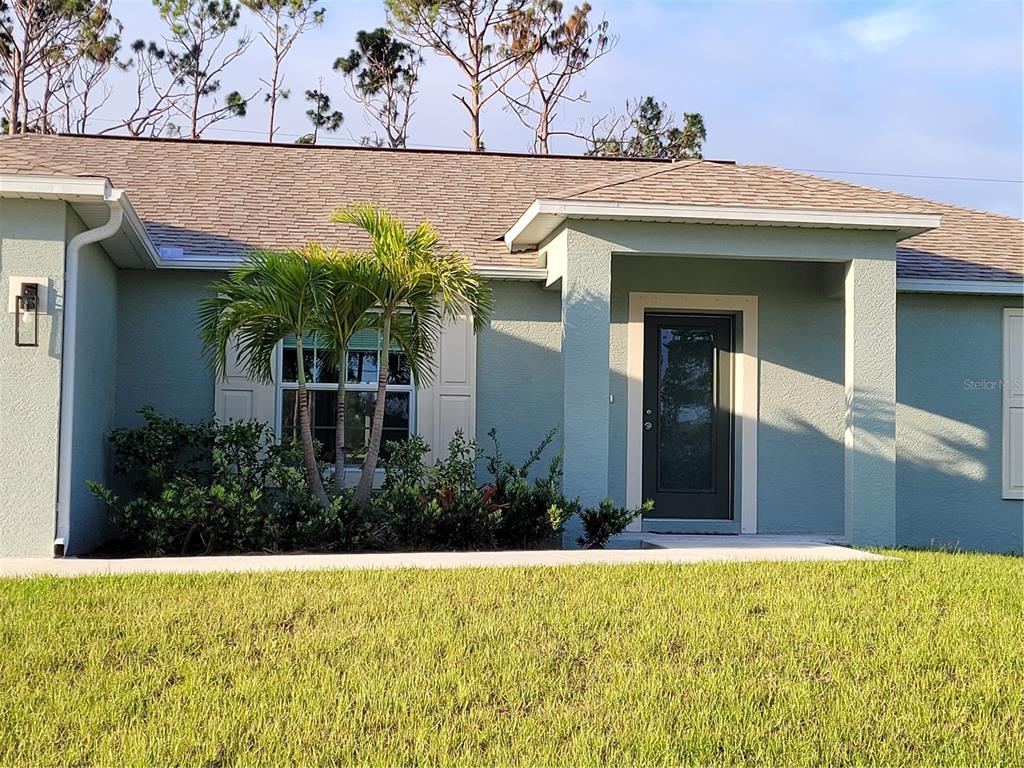 A light green house exterior features a front door, a window with shutters, and landscaping — 13481 DRYSDALE AVENUE, PORT CHARLOTTE, FL