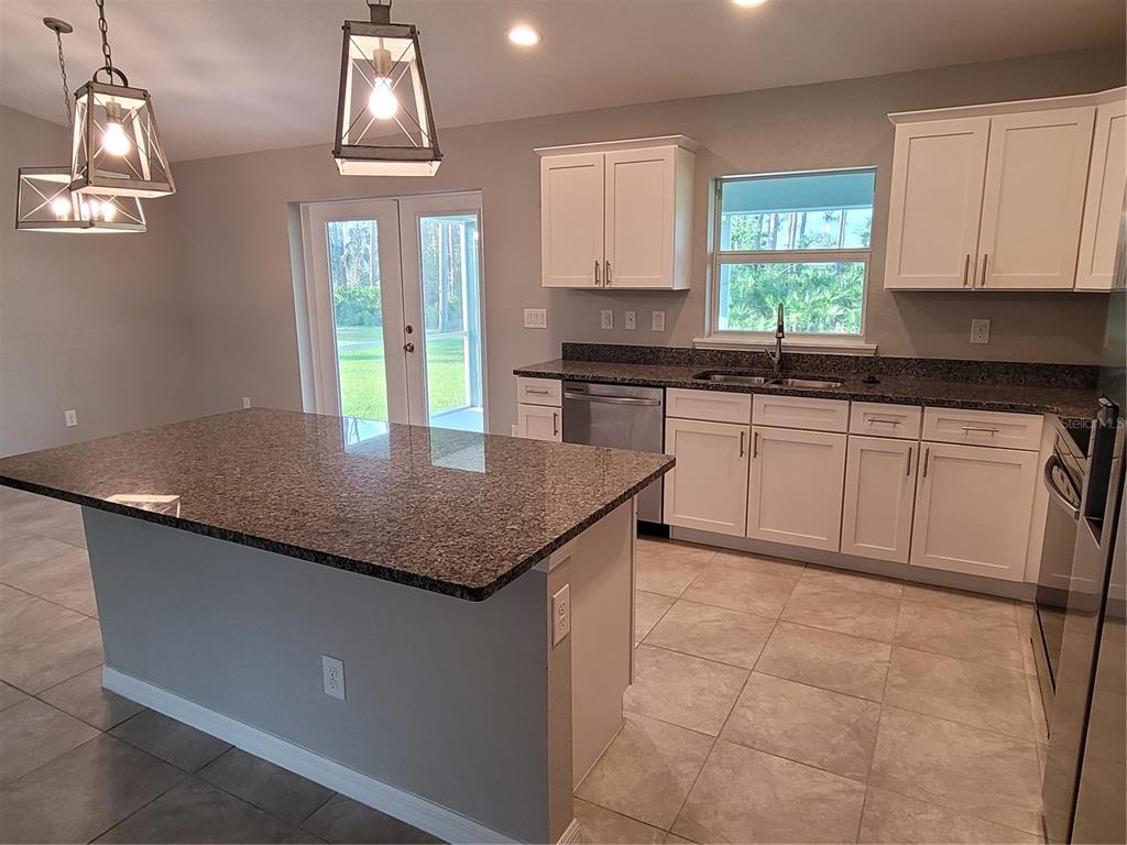 A kitchen features white cabinets, granite countertops, a center island, and pendant lighting — 13481 DRYSDALE AVENUE, PORT CHARLOTTE, FL