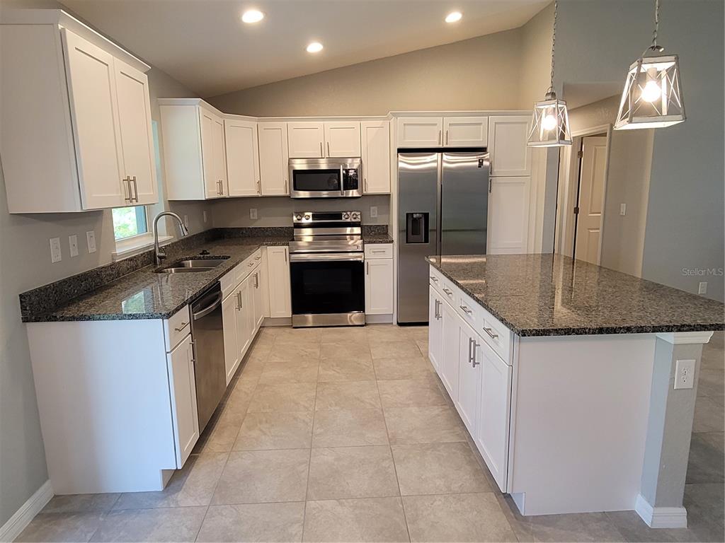A kitchen features white cabinets, granite countertops, stainless steel appliances, and a central island — 13481 DRYSDALE AVENUE, PORT CHARLOTTE, FL