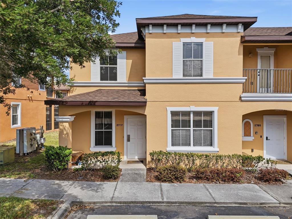 A two-story tan stucco townhouse with a covered entryway and a small front garden — 2707 CAMARO DRIVE, KISSIMMEE, FL