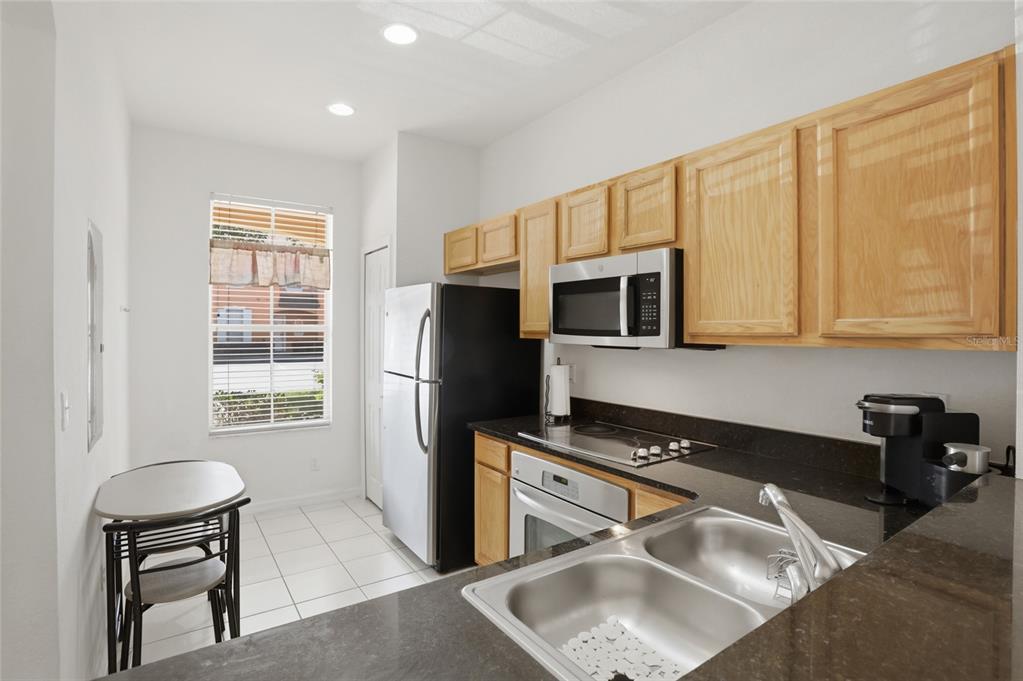 A kitchen features light wood cabinets, dark countertops, stainless steel appliances, and a small dining area — 2707 CAMARO DRIVE, KISSIMMEE, FL