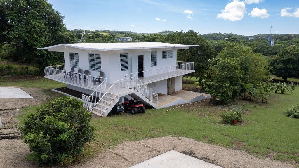 An elevated white house with a wrap-around balcony and external stairs sits on a grassy lot — 595 COMM. VILLA BORINQUEN, VIEQUES, PR
