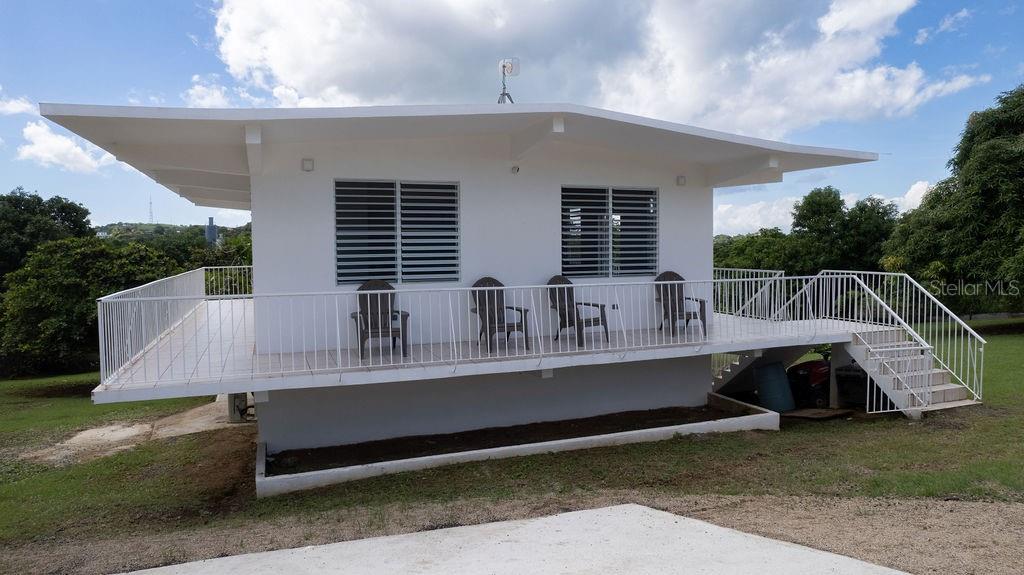 A white, elevated house features a wrap-around balcony with metal railings and louvered windows — 595 COMM. VILLA BORINQUEN, VIEQUES, PR
