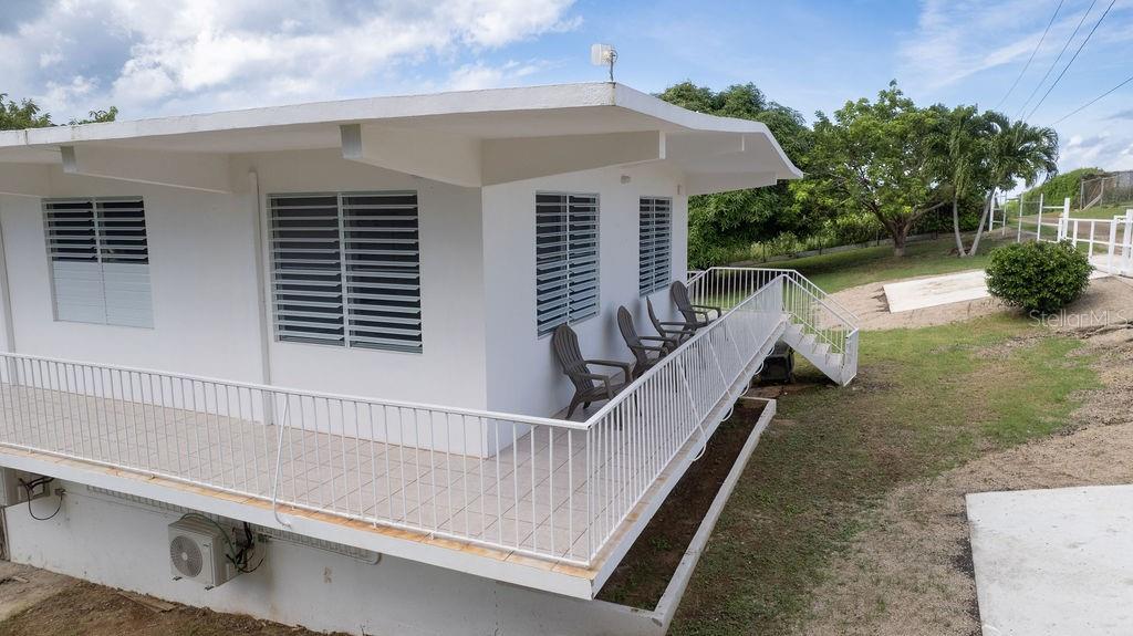 An elevated white house features a wraparound balcony with a metal railing and outdoor chairs — 595 COMM. VILLA BORINQUEN, VIEQUES, PR