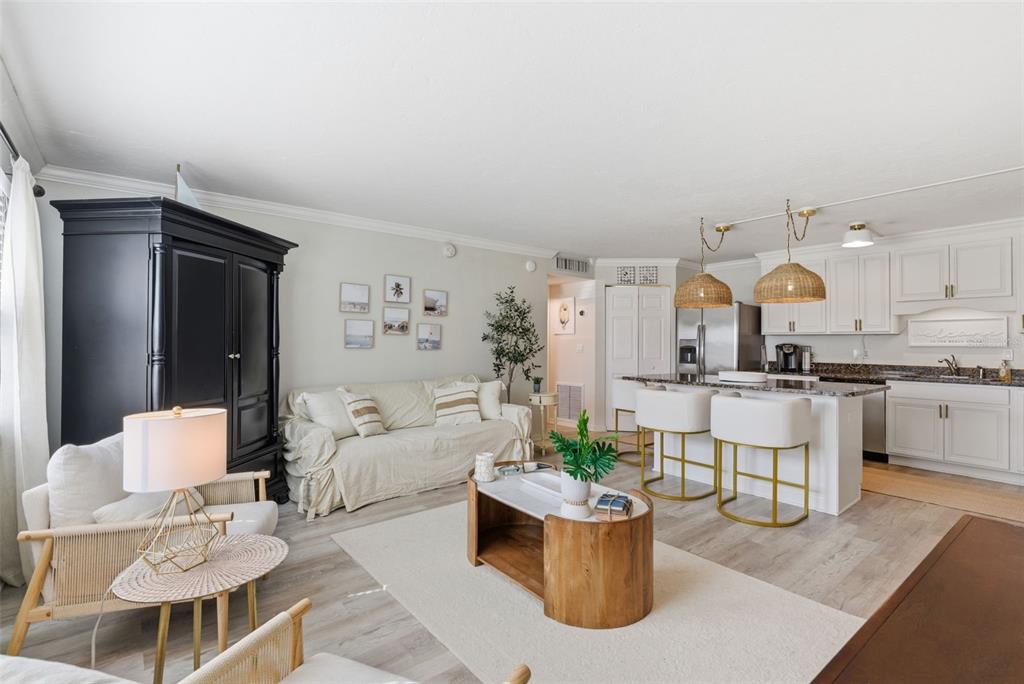 An open-concept living room and kitchen feature light wood floors, white cabinetry, and neutral furniture — 5800 HOLLYWOOD BOULEVARD UNIT 214, SARASOTA, FL