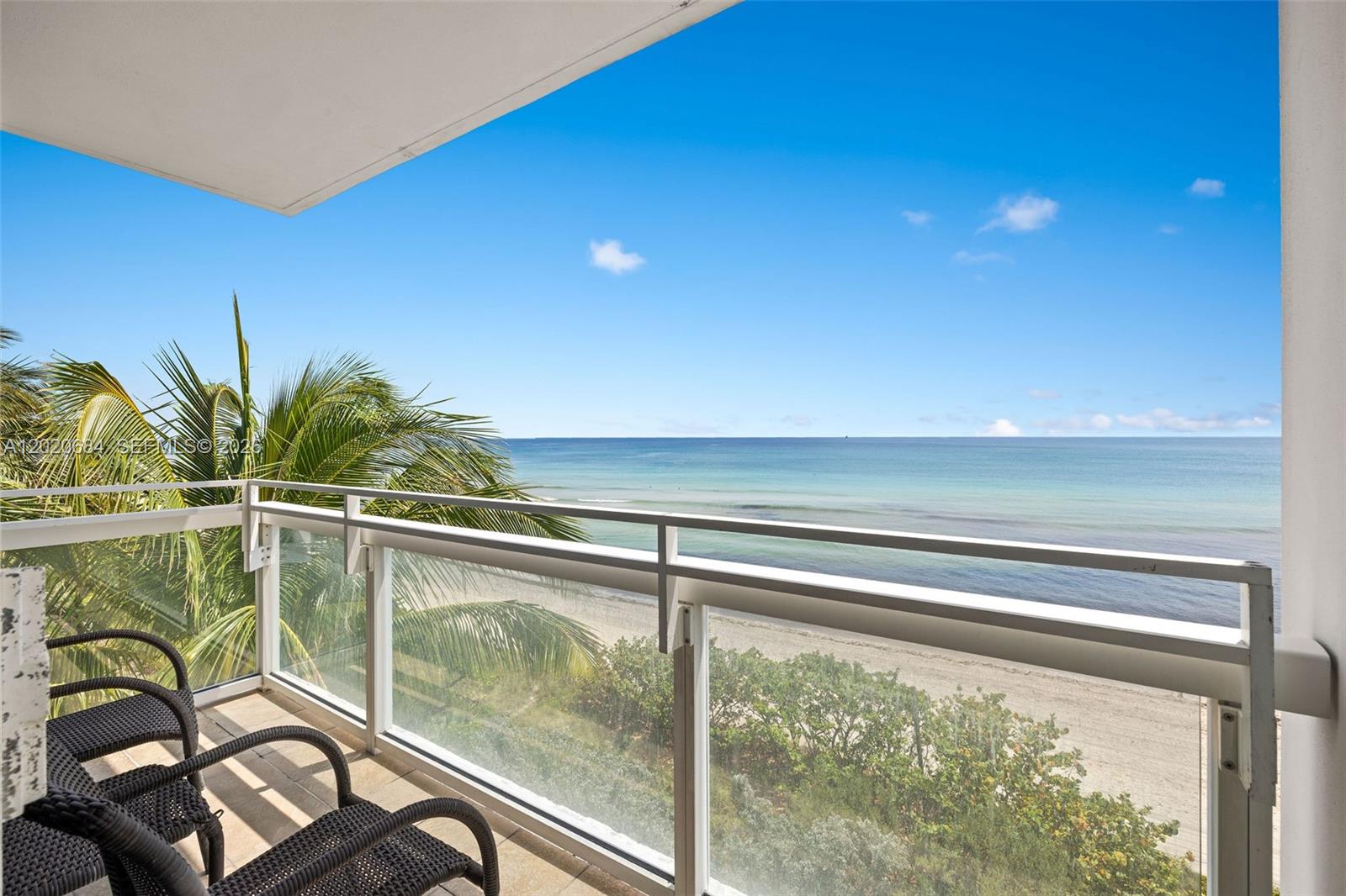 A balcony with wicker chairs overlooks a sandy beach and the ocean — 6801 Collins Ave # 417, Miami Beach FL 33141, MIAMI BEACH, FL