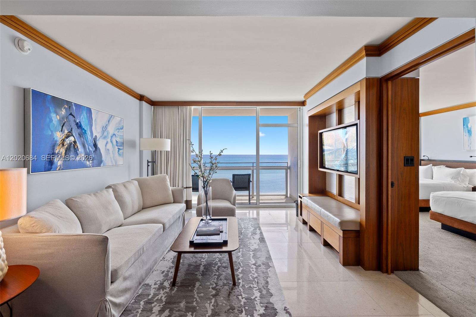 A living room with a beige sofa, wooden media unit, and ocean view balcony — 6801 Collins Ave # 417, Miami Beach FL 33141, MIAMI BEACH, FL