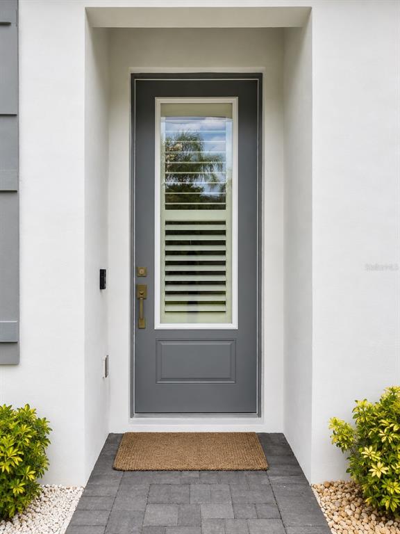 A gray front door with a glass insert and shutters sits in a white entryway — 3079 ISLES WAY, NEW SMYRNA BEACH, FL
