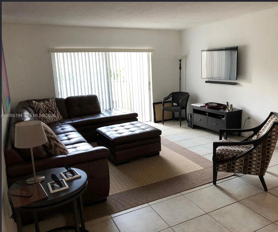 A living room features a brown leather sectional, a matching ottoman, and tile flooring — 7705 SW 86th St # 211, Miami FL 33143, MIAMI, FL