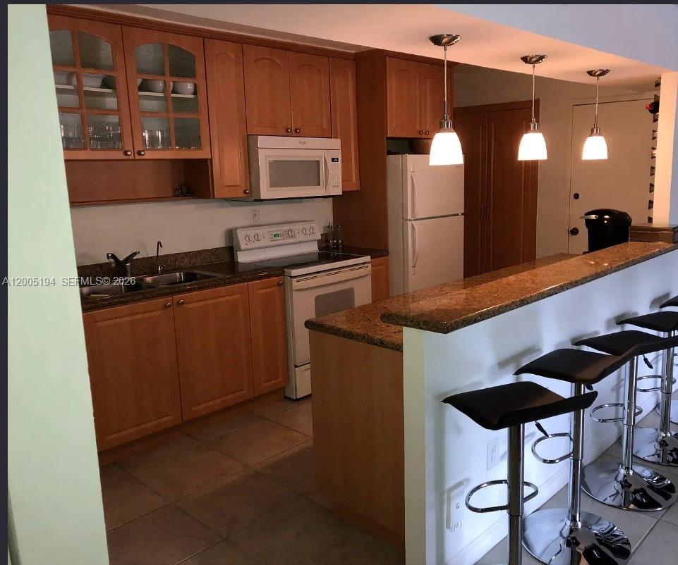 A kitchen with wood cabinets, granite countertops, and a breakfast bar with three stools — 7705 SW 86th St # 211, Miami FL 33143, MIAMI, FL