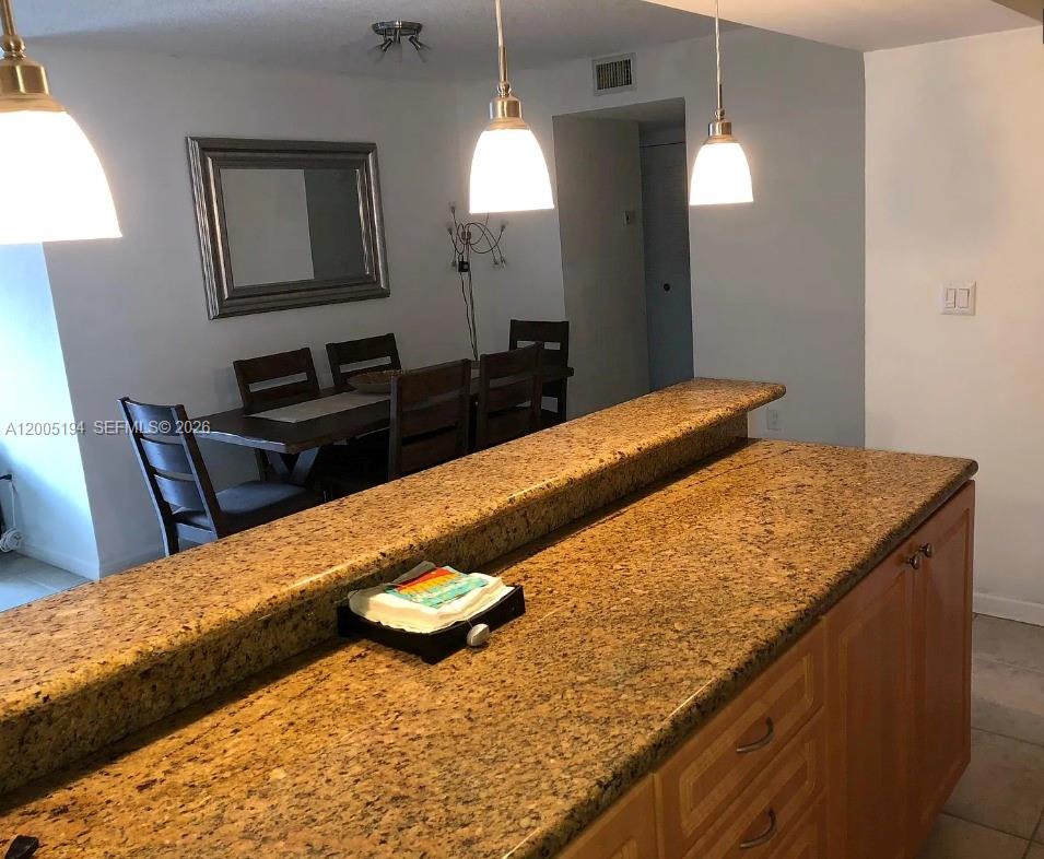 A kitchen island with a granite countertop overlooks a dining area with wooden furniture — 7705 SW 86th St # 211, Miami FL 33143, MIAMI, FL