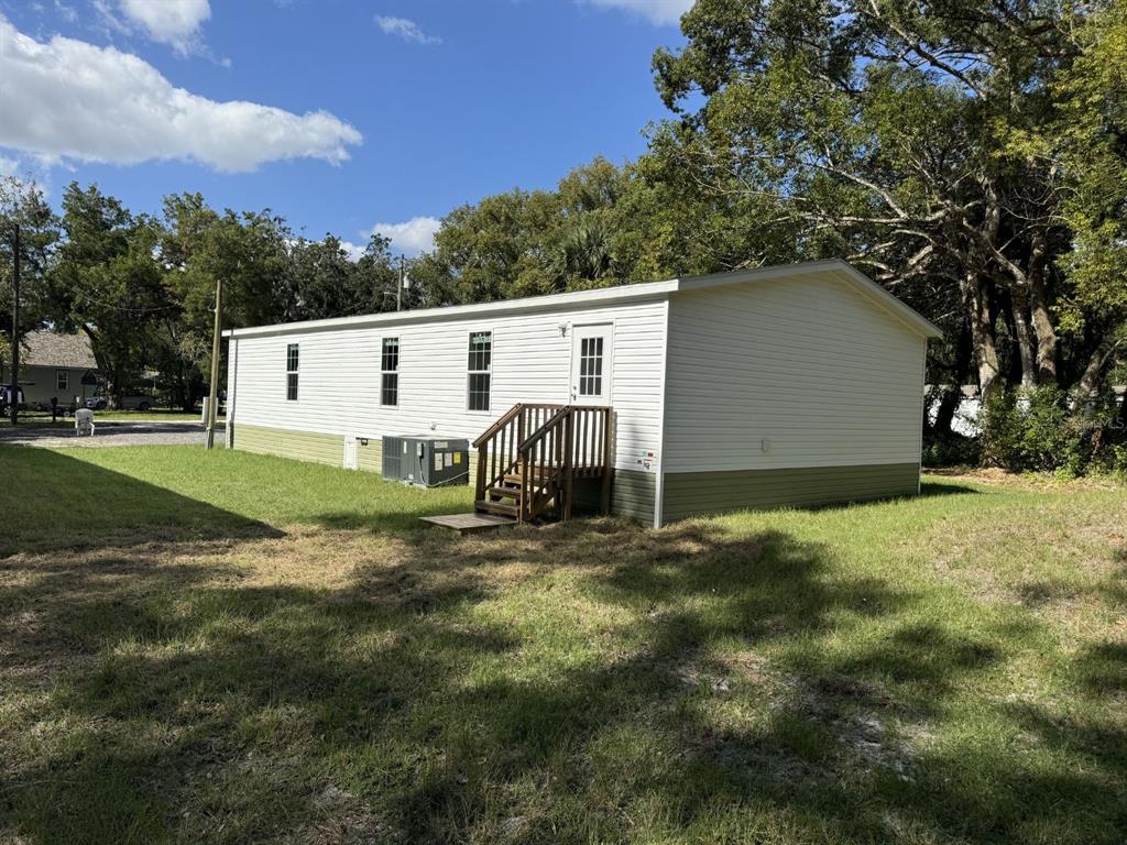 A white mobile home with green skirting and wooden stairs sits on a grassy lot — 10226 MARKHAM STREET, NEW PORT RICHEY, FL