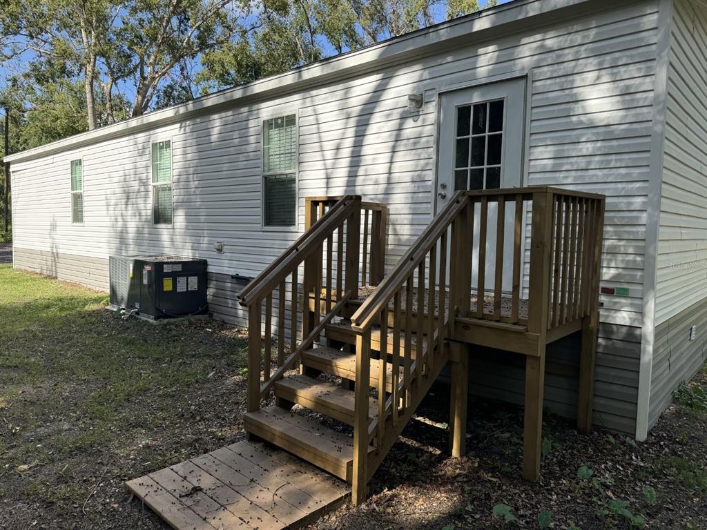 An exterior view of a mobile home featuring white siding, a wooden deck, and stairs — 10226 MARKHAM STREET, NEW PORT RICHEY, FL