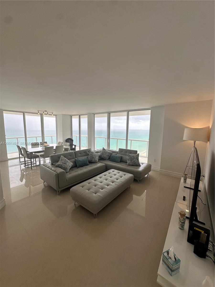 A living and dining area features light tile floors, a gray sectional, and ocean views — 6365 Collins Ave # 1703, Miami Beach FL 33141, MIAMI BEACH, FL