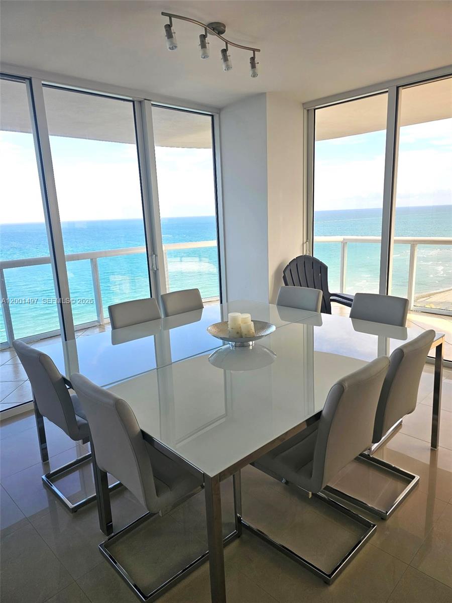 A dining room features a glass-topped table, six chairs, and floor-to-ceiling windows overlooking the ocean — 6365 Collins Ave # 1703, Miami Beach FL 33141, MIAMI BEACH, FL