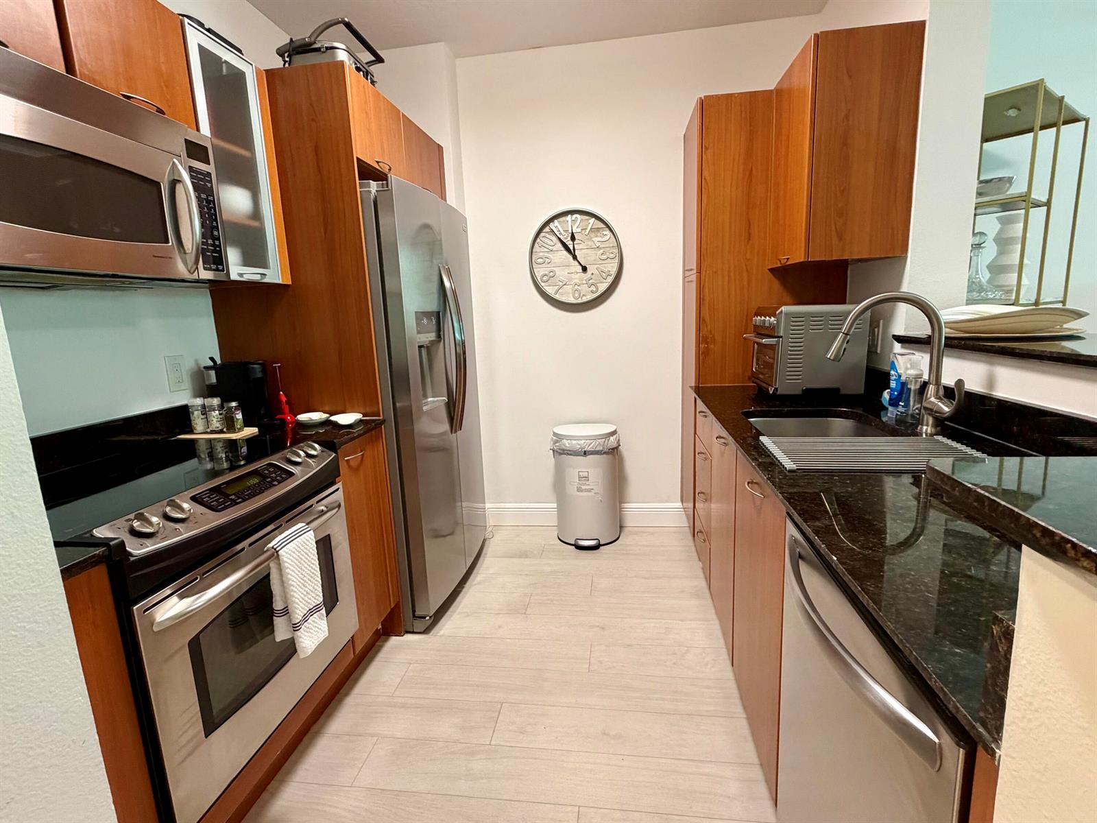 A galley kitchen features wood cabinets, stainless steel appliances, and dark granite countertops — 625 Casa Loma Boulevard # 207, Boynton Beach FL 33435, BOYNTON BEACH, FL