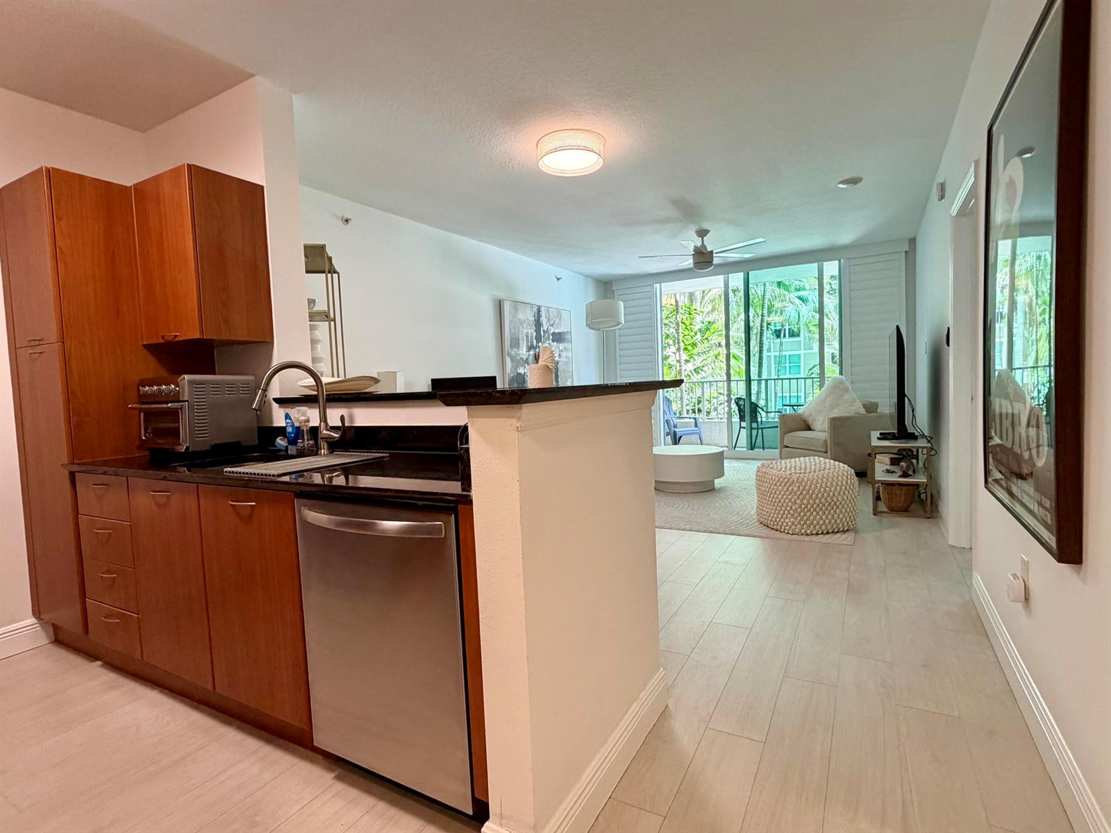A kitchen with wooden cabinets and a stainless steel dishwasher opens into a living area — 625 Casa Loma Boulevard # 207, Boynton Beach FL 33435, BOYNTON BEACH, FL