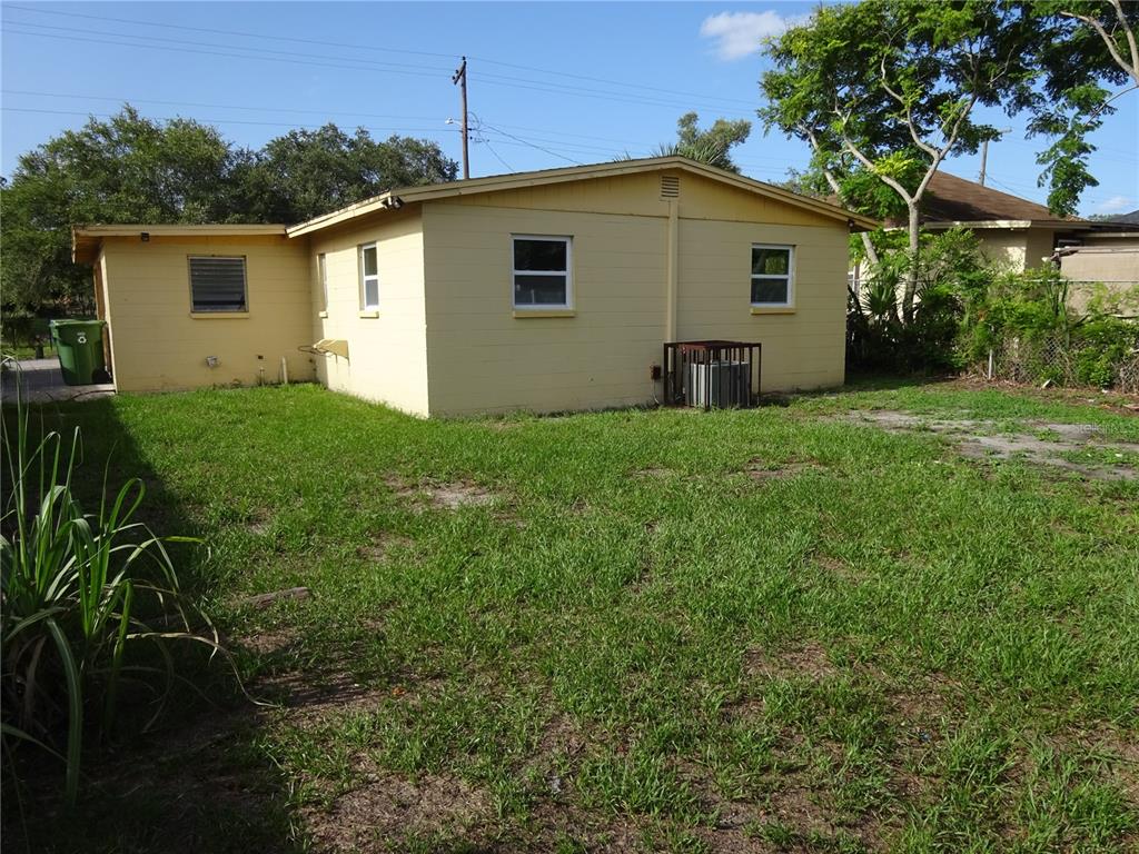 The exterior of a yellow, single-story house with a grassy backyard and an air conditioning unit — 4307 E OSBORNE AVENUE, TAMPA, FL