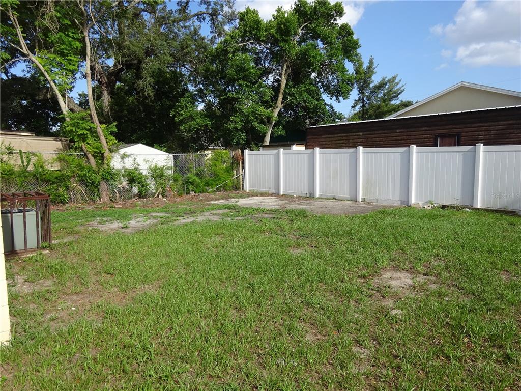 A grassy backyard features a concrete slab, a white vinyl fence, and mature trees — 4307 E OSBORNE AVENUE, TAMPA, FL