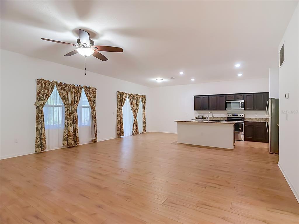 An open-concept living area features light wood-look flooring, a ceiling fan, and a kitchen — 1120 TOBIE ST, LAKE WALES, FL