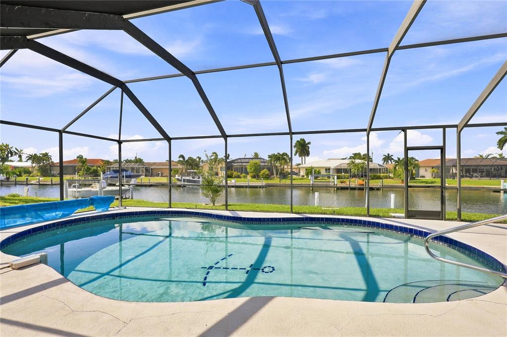 A screened-in swimming pool overlooks a canal with boat docks and neighboring houses — 425 BELVEDERE COURT, PUNTA GORDA, FL