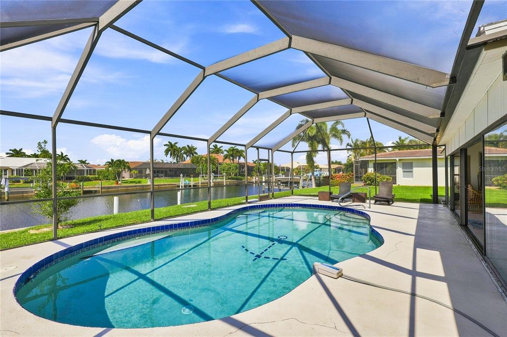 A screened-in pool patio overlooks a canal with neighboring houses in the background — 425 BELVEDERE COURT, PUNTA GORDA, FL