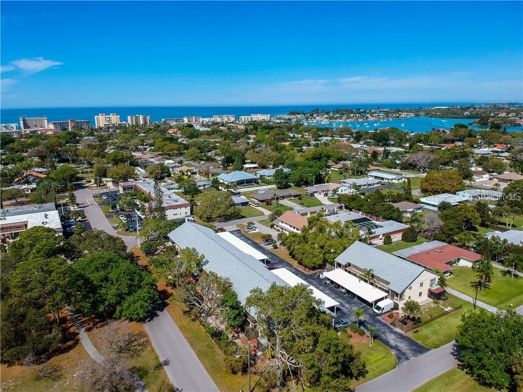 An aerial view shows multi-family residential buildings, surrounding trees, and a distant coastal waterway — 525 PARKDALE UNIT 525, VENICE, FL