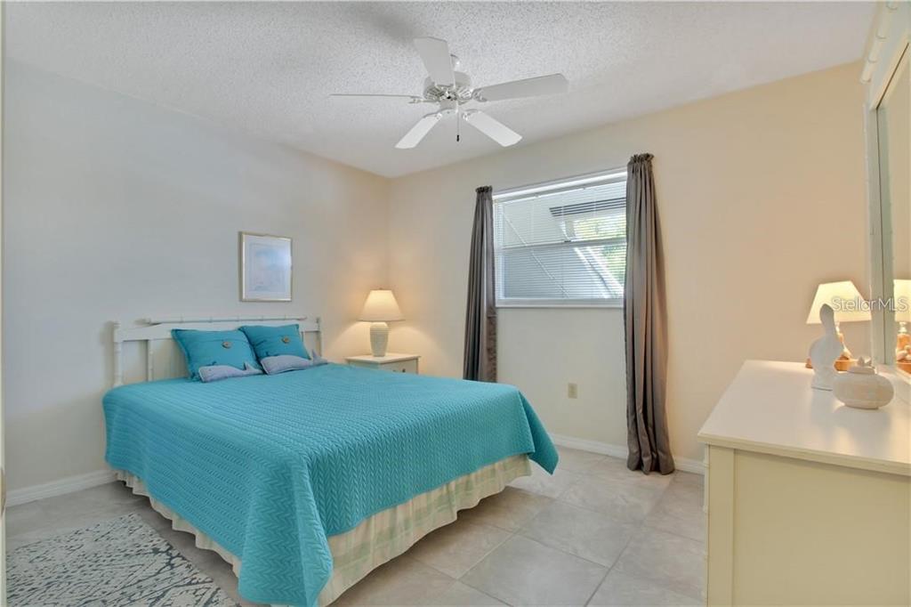 A bedroom features a turquoise bedspread, a ceiling fan, a window with curtains, and tile flooring — 525 PARKDALE UNIT 525, VENICE, FL