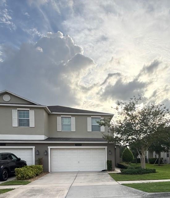 A two-story townhouse features a two-car garage, light-colored siding, and a cloudy sky above — 15054 HARRINGTON COVE DRIVE, ORLANDO, FL