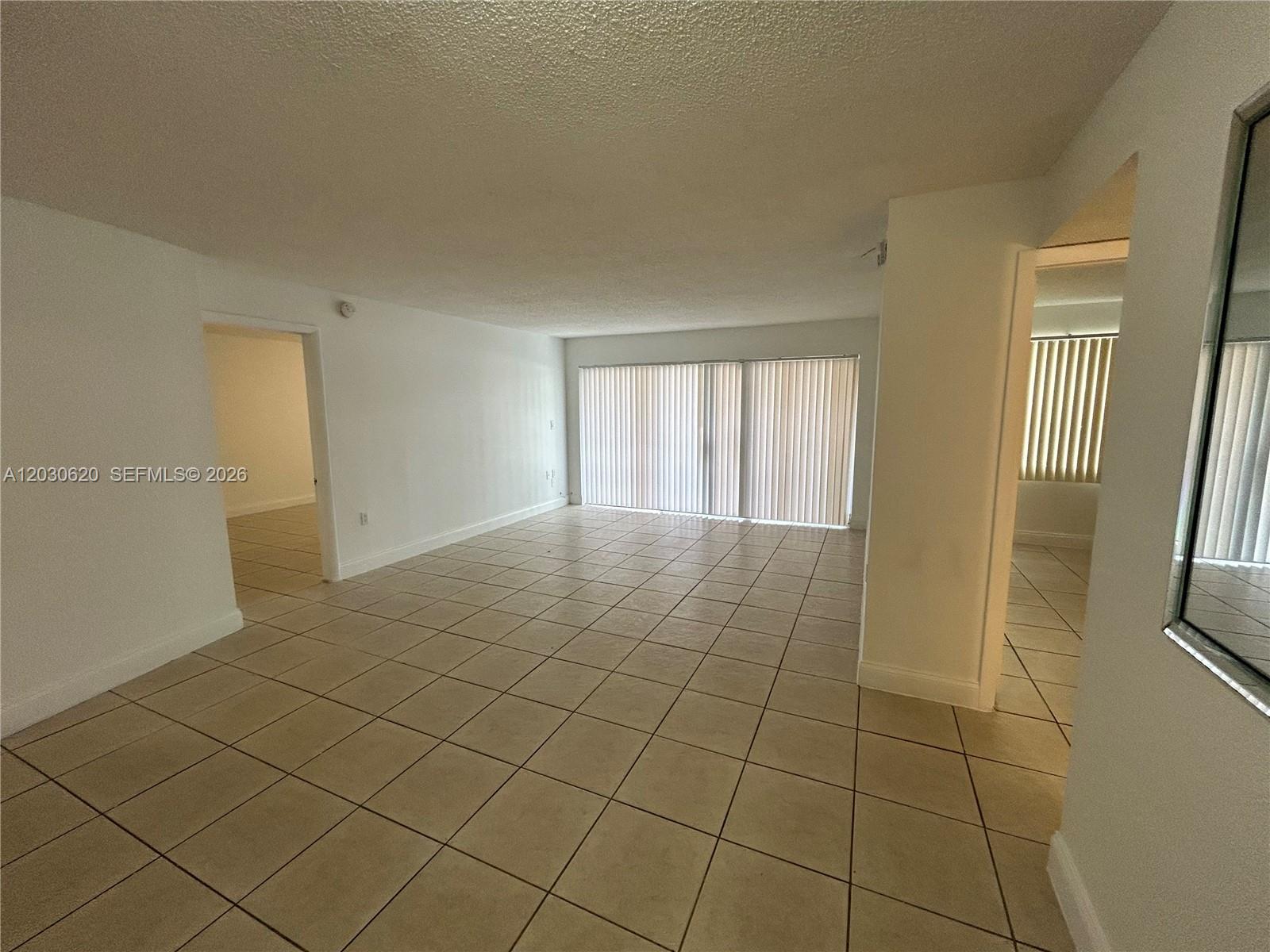 An empty living room features light-colored tile flooring, white walls, and large sliding glass doors — 4205 N University Dr # 112, Sunrise FL 33351, SUNRISE, FL