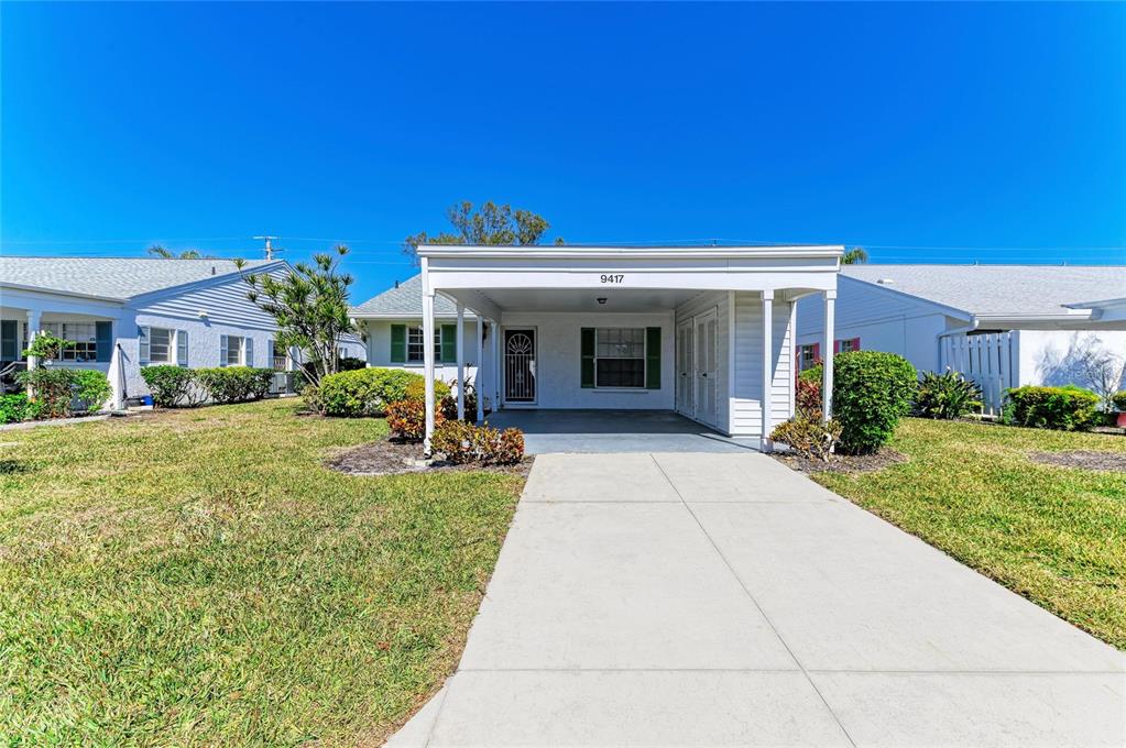 A single-story house features a white exterior, a front carport, and a concrete driveway — 9417 KINGSTON DRIVE UNIT 9417, BRADENTON, FL