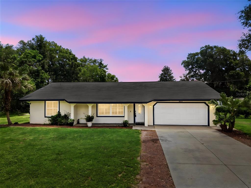 A single-story house with a white exterior, dark trim, and a two-car garage at sunset — 535 LAND O LAKES COURT, DELAND, FL