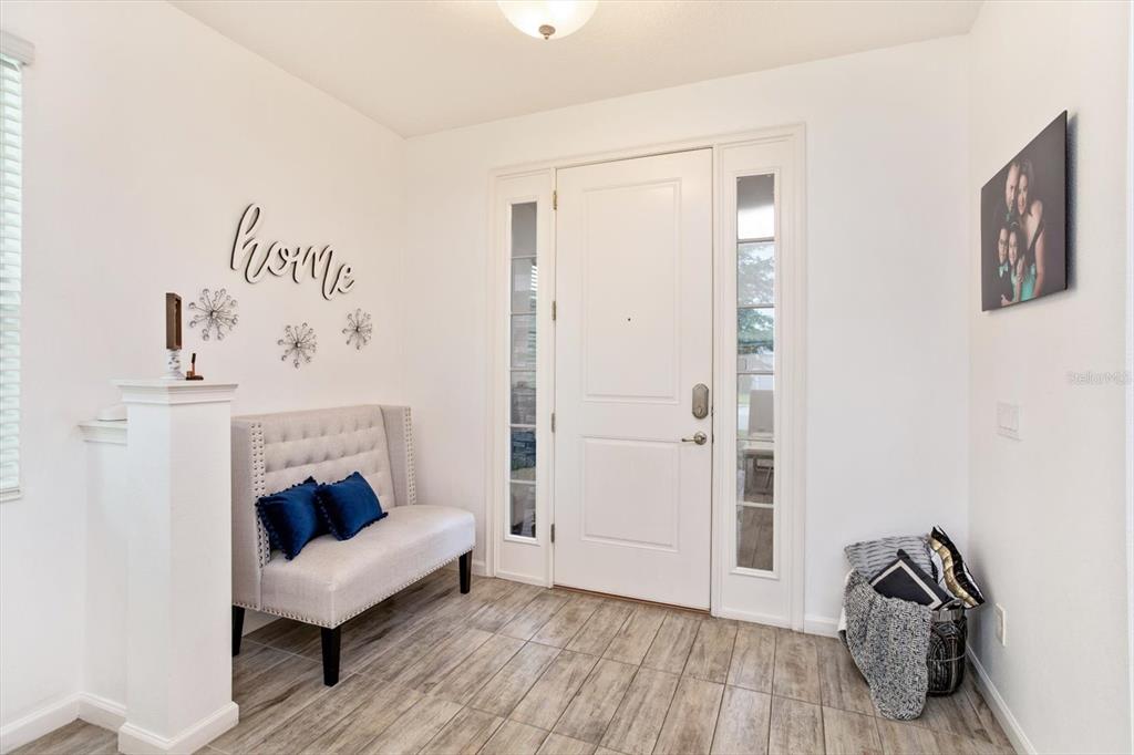 An entryway features a white front door, a tufted bench, and wood-look tile flooring — 1324 YORKDALE ROAD, DAVENPORT, FL