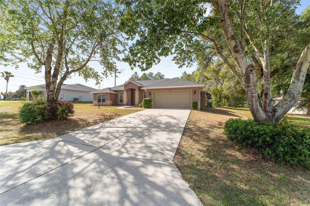 A single-story house with a beige exterior, stone accents, and a concrete driveway under trees — 5061 SW 109TH LOOP, OCALA, FL