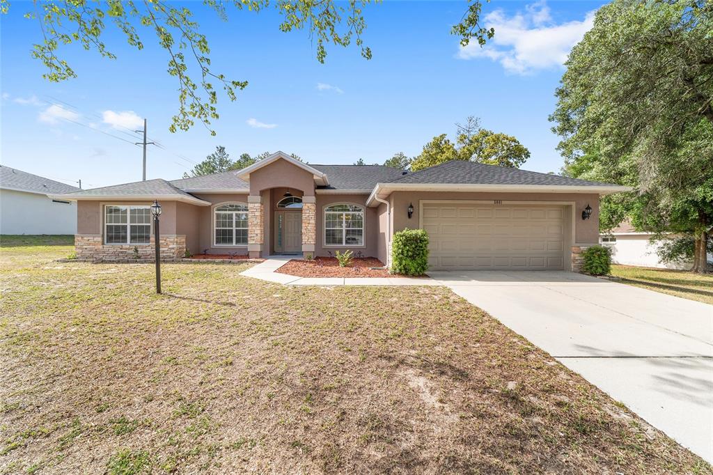 A single-story house with a tan stucco exterior, stone accents, and an attached two-car garage — 5061 SW 109TH LOOP, OCALA, FL