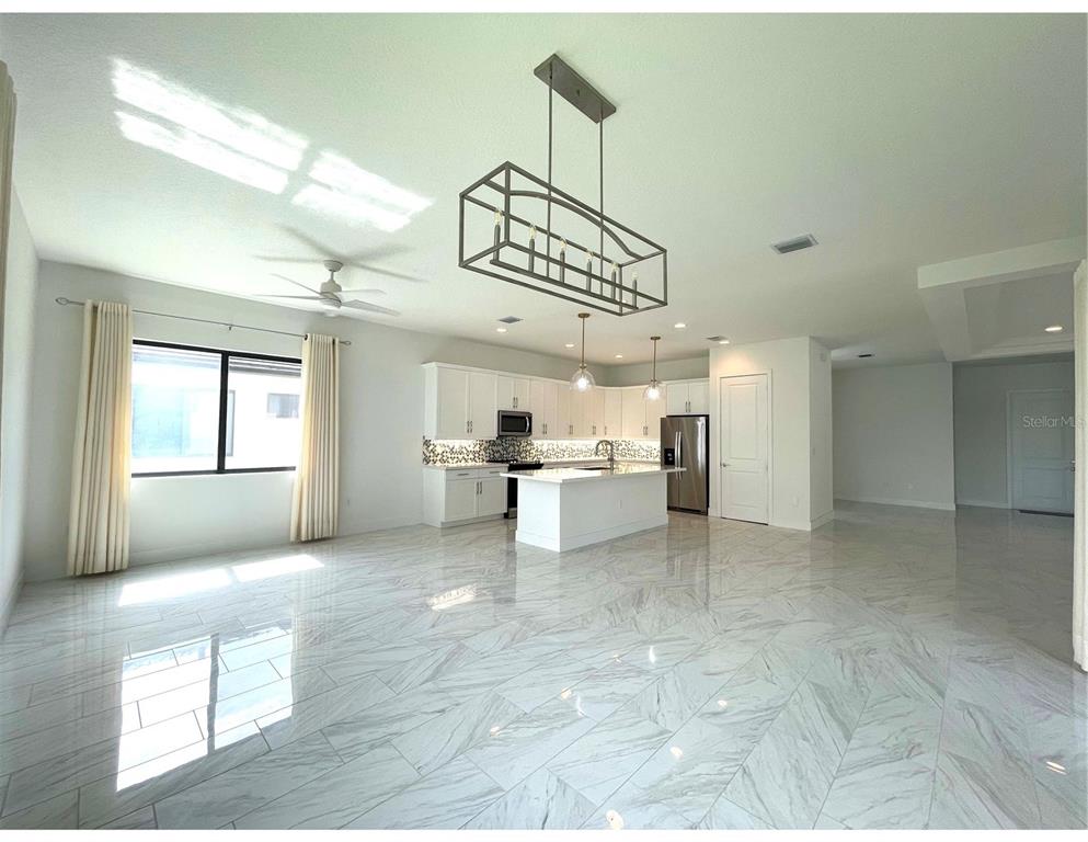 A bright, open-concept kitchen features white cabinetry, a central island, and polished marble-look flooring — 4959 BRIGATA WAY, IMMOKALEE, FL