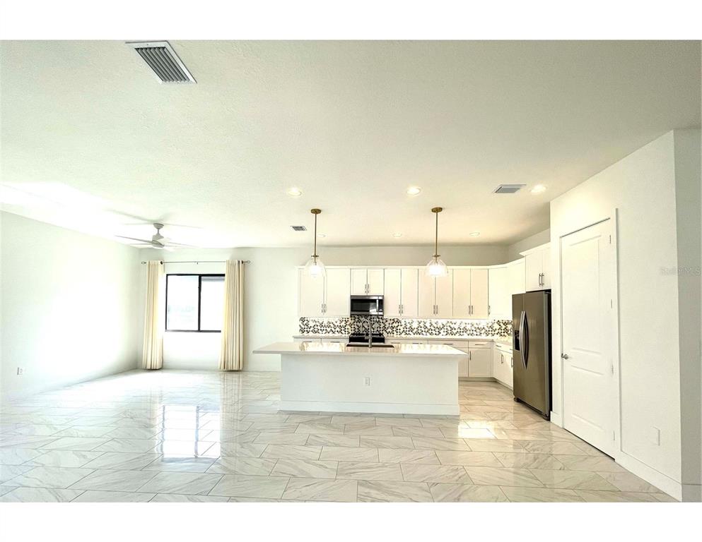 A bright, open-concept kitchen features white cabinetry, a central island, and light-colored tile flooring — 4959 BRIGATA WAY, IMMOKALEE, FL