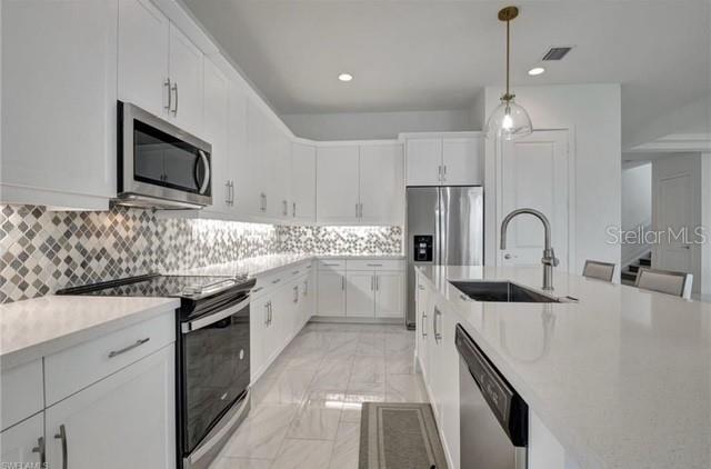 A modern kitchen features white cabinets, stainless steel appliances, and a large quartz island — 4959 BRIGATA WAY, IMMOKALEE, FL